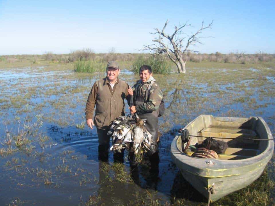 Guía y cazador con patos en un bañado poco profundo